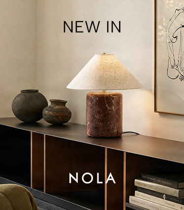 Stolní lampa Nola s červenohnědým mramorovým podstavcem a kónickým lněným stínidlem na tmavém příborníku. Text: „Novinka – Nola“.