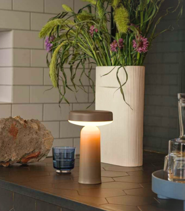 Přenosná stolní lampa Ease od Muuto na tmavé kuchyňské pracovní desce s květinovou dekorací.