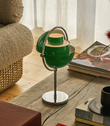 Zelená stolní lampa Multi-Lite s chromovanou základnou na dřevěném stole vedle knih.